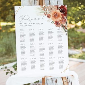Op de afbeelding: Een zitplaatskaart voor een bruiloft met een bloemenontwerp met oranje, rode en witte bloemen. De kaart is getiteld "Find your seat" en vermeldt de namen van de gasten die aan elke tafel zijn toegewezen. De tekst luidt "Olivia & Theodore, June 19th, 2006."