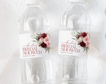 May include: Two clear plastic water bottles with labels that say "Amelia's Bridal Shower" with a floral design in shades of burgundy, pink, and green. The text on the labels also says "August 19, 2026".
