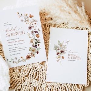 May include: Two white cards with floral designs and the text "bridal shower" in a copper color. The card on the left has the text "Olivia Johnson" and the date "May 15th at 5:00pm". The card on the right has the text "Olivia's Bridal Shower" and the date "May 15th, 2023".