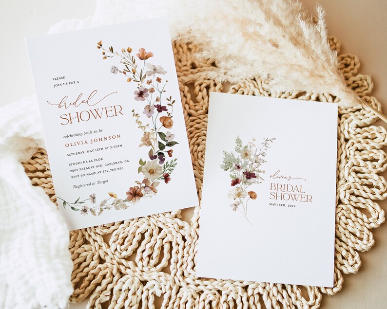 May include: Two white cards with floral designs and the text "bridal shower" in a copper color. The card on the left has the text "Olivia Johnson" and the date "May 15th at 5:00pm". The card on the right has the text "Olivia's Bridal Shower" and the date "May 15th, 2023".