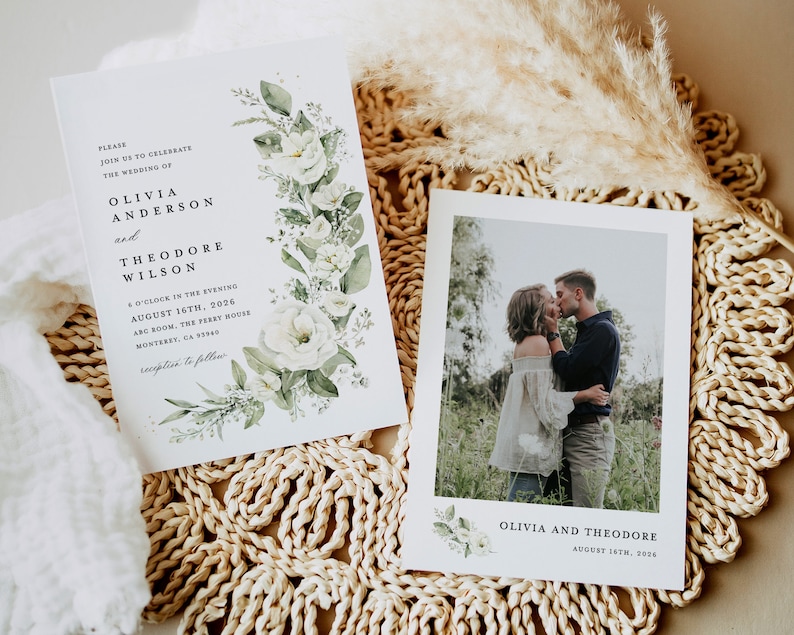 May include: A wedding invitation with white flowers and green leaves on a white background. The invitation reads "Please join us to celebrate the wedding of Olivia Anderson and Theodore Wilson 6 o'clock in the evening August 16th, 2026 ABC Room, The Perry House Monterey, CA 93940 reception to follow". A photo of the couple kissing is on a separate card with the text "Olivia and Theodore August 16th, 2026".