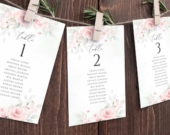 May include: Three floral-themed table cards with the words "Table 1", "Table 2", and "Table 3" and a list of names for each table. The cards are decorated with pink and green watercolor flowers.