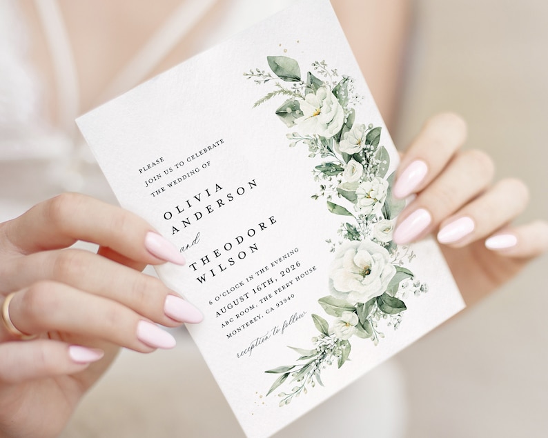 May include: White wedding invitation with green foliage and white flowers. The invitation reads "Please join us to celebrate the wedding of Olivia Anderson and Theodore Wilson 6 o'clock in the evening August 16th, 2026 ABC Room, The Ferry House Monterey, CA 93940 reception to follow"