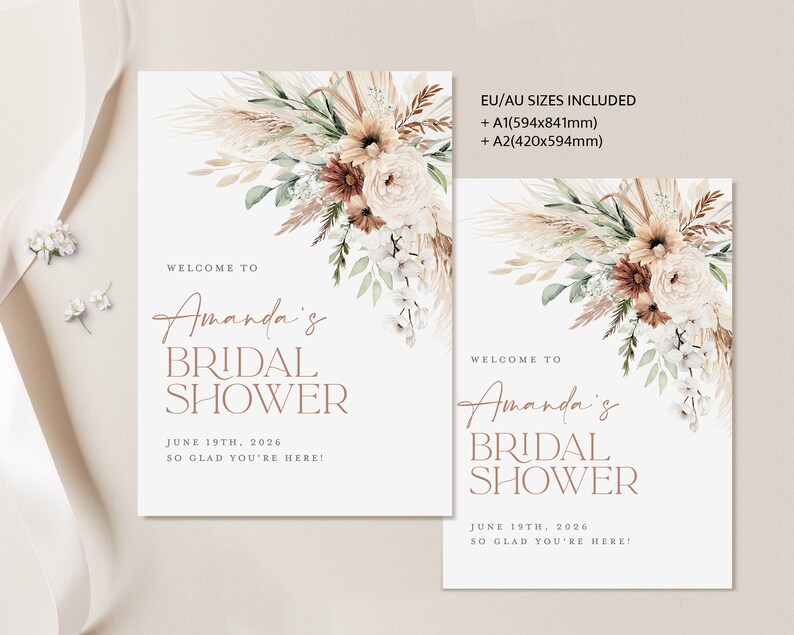 Op de afbeelding: Twee witte rechthoekige borden met bloemstukken en tekst. De borden luiden "Welkom bij Amanda's Bridal Shower" met de datum "19 juni 2026". Het grotere bord bevat EU/AU-maatinformatie. De bloemstukken bevatten beige, bruine en witte bloemen.