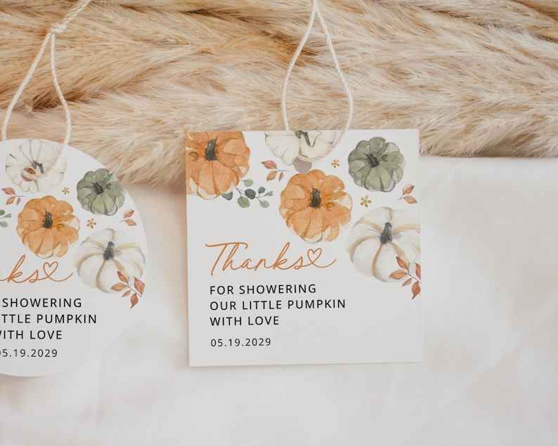 May include: Two round white tags with a watercolor design of pumpkins and leaves. The text on the tags reads "Thanks for showering our little pumpkin with love 05.19.2029" and "kse showering little pumpkin with love 05.19.2029".