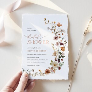 May include: A floral bridal shower invitation with a watercolor design of flowers in shades of pink, orange, and yellow. The text reads "Please join us for a bridal shower celebrating bride-to-be Olivia Johnson Saturday, May 16th at 5:00PM Studio de la Flor 2205 Faraday Ave, Carlsbad, CA RSVP to name at 532.783.226 Registered at Target"