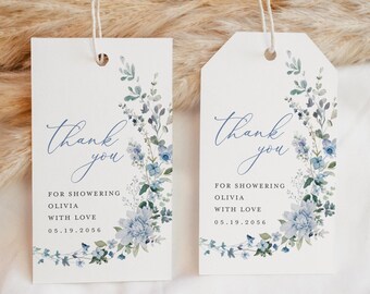 Op de afbeelding: Twee witte cadeaulabels met een bloemenontwerp. De labels hebben een blauwe bloemenkrans en de woorden "Thank you" in cursief. De tekst hieronder luidt "FOR SHOWERING OLIVIA WITH LOVE 05.19.2056". Elk label is rechthoekig en heeft een touwtje.