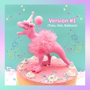 May include: A pink Tyrannosaurus Rex figurine wearing a pink tulle tutu and a party hat, holding a pink balloon, standing on a frosted cake. The text Version #1 (Tutu, Hat, Balloon) is visible above the dinosaur against a teal background.