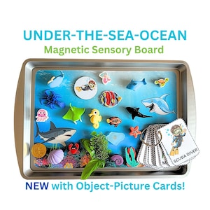 Op de afbeelding: Een rechthoekig metalen dienblad met een magnetisch sensorisch bord met een oceaanthema. Het bevat diverse kleurrijke magneten van zeedieren, waaronder haaien, een rog, een krab en een zeepaardje, naast een set object-afbeeldingskaarten aan een ring.