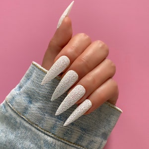 K&ouml;nnte beinhalten: Wei&szlig;e Stiletto-N&auml;gel mit glitzerndem Finish.