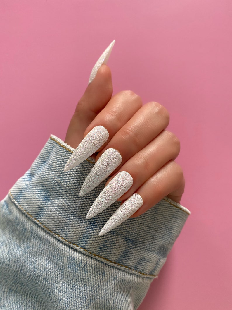 K&ouml;nnte beinhalten: Wei&szlig;e Stiletto-N&auml;gel mit glitzerndem Finish.