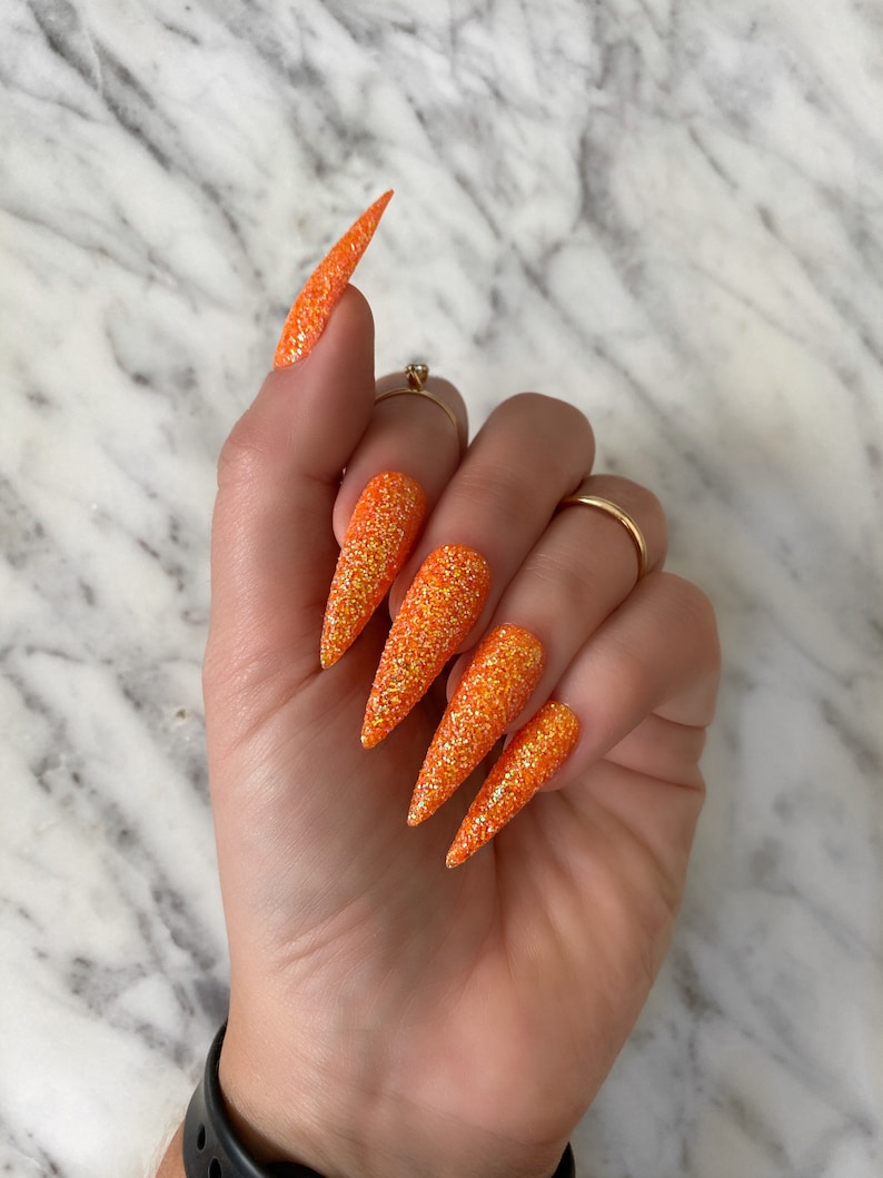 Op de afbeelding: Oranje glitter stiletto valse nagels. De nagels zijn lang en puntig, met een glinsterende afwerking.
