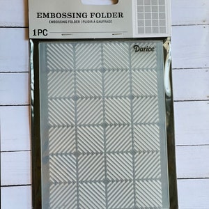 May include: A clear plastic embossing folder with a geometric pattern of diagonal lines in a grid. The folder is packaged in a clear plastic bag with a white header card that reads "Embossing Folder" and "Darice".