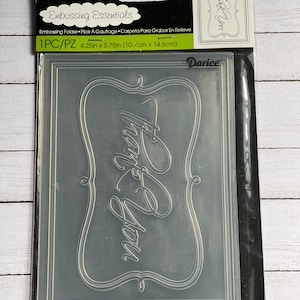 May include: A clear plastic embossing folder with a decorative frame and the text "Thank You" inside. The folder measures 4.25 inches by 5.75 inches.