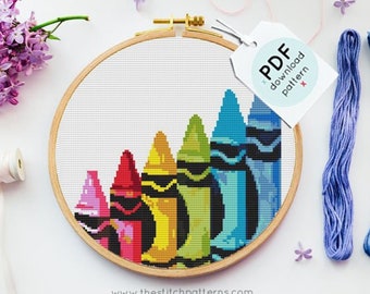 May include: A cross-stitch pattern of a row of colorful crayons in a wooden embroidery hoop. The pattern is available as a PDF download. The image also shows four skeins of embroidery floss in shades of blue, pink, and gray.