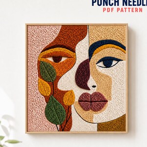 Op de afbeelding: Een vierkant punch needle wandkunstwerk met een abstract gezichtontwerp in getextureerd garen. De compositie gebruikt een palet van roze, roest, mosterd, marineblauw, crème en groen, met bladmotieven en de tekst PUNCH NEEDLE PDF PATTERN.