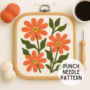 May include: A square punch needle pattern featuring three orange flowers with green leaves on a white background, set in a wooden embroidery hoop. The text "PUNCH NEEDLE PATTERN" is visible. Includes orange and white yarn.