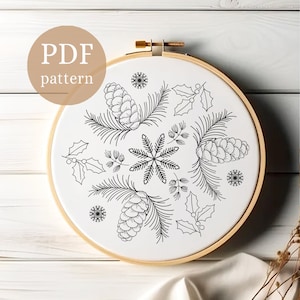 Może przedstawiać: Wzór do haftu czarno-białego na wieniec bożonarodzeniowy z gałązkami sosny, szyszkami, liśćmi ostrokrzewu i płatkami śniegu. Wzór jest przedstawiony w okrągłym tamborku do haftu.