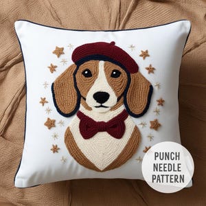 Puede incluir: Almohada blanca con un diseño de aguja de punzón de un perro marrón y blanco que lleva una boina roja y una pajarita roja. El perro está rodeado de estrellas doradas. El texto "PUNCH NEEDLE PATTERN" está en la esquina inferior derecha de la almohada.