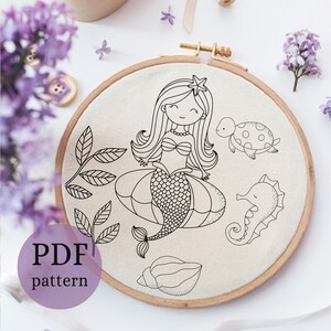 May include: A black and white embroidery pattern featuring a mermaid with a star on her head, a seahorse, a turtle, and seashells. The pattern is on a white fabric background.