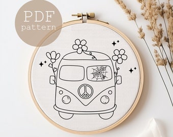 May include: Black and white embroidery pattern of a vintage van with flowers and a spider web in the window. The pattern is on a white fabric background in a round embroidery hoop.