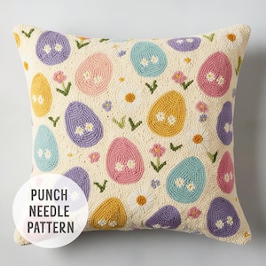 Puede incluir: Una almohada blanca con un patrón de huevos de Pascua y flores de colores hecho con aguja de punzón. El texto "Punch Needle Pattern" está en la esquina inferior izquierda de la almohada.