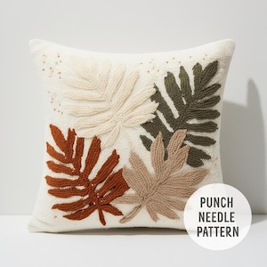 May include: Square off-white decorative pillow with a punch needle pattern featuring four large leaf designs in cream, brown, rust, and olive green. The pillow has a textured surface and the text "PUNCH NEEDLE PATTERN" in a white circle.