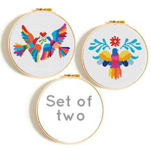 May include: Set of two embroidery hoops with colorful cross-stitch designs. One hoop features two birds with a heart and leaves, the other features a bird with a flower and leaves. The hoops are labeled "Set of two".