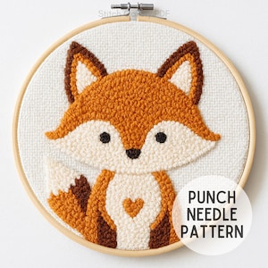 Puede incluir: Un patrón de aguja mágica de un zorro en un bastidor de bordado de madera. El zorro tiene pelaje naranja, marrón y crema, con un detalle en forma de corazón en el pecho. El texto "PUNCH NEEDLE PATTERN" está en un círculo blanco.