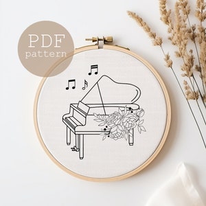 May include: Black and white line art embroidery pattern of a grand piano with musical notes and flowers. The pattern is in a hoop on a white background. PDF pattern.