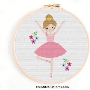 May include: Cross stitch pattern of a ballerina with a pink tutu and a crown, surrounded by colourful flowers. The pattern is displayed in a wooden embroidery hoop.