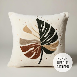 Puede incluir: Almohada blanca con un bordado de aguja de punzón de una gran hoja verde y marrón. El texto "Punch Needle Pattern" está en la esquina inferior derecha de la imagen.