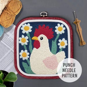 Op de afbeelding: Punch needle patroon met een witte haan met een rode kam en keellap, omringd door witte madeliefjes met gele centra op een blauwe achtergrond. Het patroon is ingelijst in een rode houten ring. De tekst "PUNCH NEEDLE PATTERN" is zichtbaar in de rechterbenedenhoek.