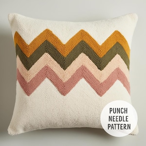 Op de afbeelding: Een wit kussen met een zigzagpatroon in tinten roze, groen en geel. Het patroon is gemaakt met een punch needle-techniek. De tekst "PUNCH NEEDLE PATTERN" is zichtbaar in de rechterbenedenhoek van de afbeelding.