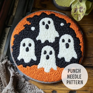 May include: A round, handmade Halloween-themed punch needle pattern featuring four white ghost figures against a black background. The design is set within an orange border and a gray edge. The text "PUNCH NEEDLE PATTERN" is in a white circle.