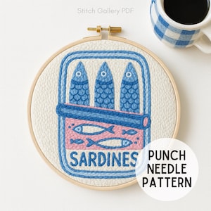 Könnte beinhalten: Ein Stickrahmen mit einem Sardinendosen-Design. Die Dose ist blau und rosa, mit drei blauen Fischen und dem Wort "SARDINES" in Weiß. Der Text "PUNCH NEEDLE PATTERN" befindet sich in einem weißen Kreis.
