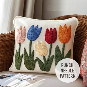 May include: A white pillow with a punch needle embroidery design of five colorful tulips. The tulips are pink, blue, red, orange, and yellow. The pillow has the text "Punch Needle Pattern" on the bottom right corner.