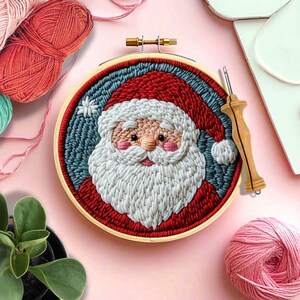 May include: A wooden embroidery hoop with a colorful yarn depiction of Santa Claus. The hoop is surrounded by yarn balls and a needle.