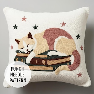 May include: A white pillow with a punch needle design of a cat sleeping on a stack of books. The cat is beige with pink accents and the books are brown, green, and beige. There are small stars scattered around the cat and books.