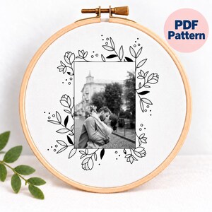 May include: A wooden embroidery hoop containing white fabric with a black and white photograph of a couple embracing, surrounded by a black line-art floral border. The text PDF Pattern is visible in a pink circle in the upper right corner.