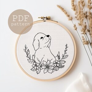 Könnte beinhalten: Schwarzweißes Linienkunst-Stickmuster eines Hündchens, das in einem Kreis aus Blumen sitzt. Das Muster ist in einem Stickrahmen und bereit zum Sticken.