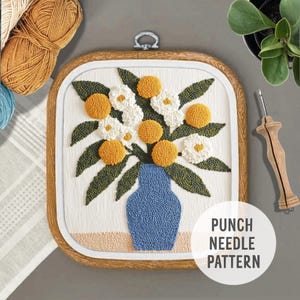 May include: A punch needle embroidery pattern featuring a bouquet of white and yellow flowers in a blue vase. The pattern is framed in a wooden hoop and includes the text "Punch Needle Pattern".