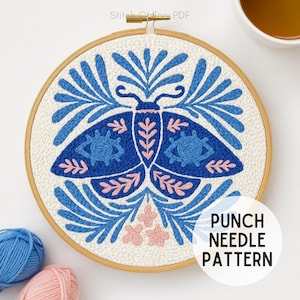 May include: A blue and white punch needle pattern featuring a moth design with eye details and floral accents. The design is set in a wooden embroidery hoop. The text "PUNCH NEEDLE PATTERN" is visible.