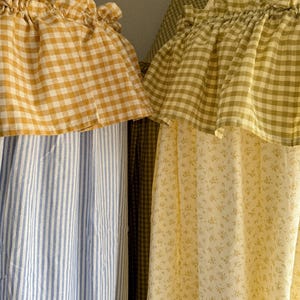 May include: Two fabric canopies featuring ruffled tops. The left canopy has blue and white vertical stripes with a yellow and white gingham ruffle. The right canopy has a yellow floral print with a green and white gingham ruffle.