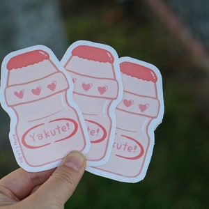 May include: Three pink and white Yakult-style yogurt drink bottle stickers with hearts and the text "Yakute!"