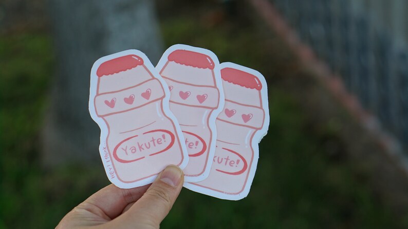May include: Three pink and white Yakult-style yogurt drink bottle stickers with hearts and the text "Yakute!"