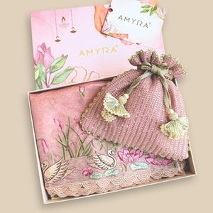 May include: A pink gift set featuring a scarf with a swan and lotus design, a matching drawstring bag, and a box with the brand name "AMYRA". The scarf is folded inside the box, and the bag is on top.