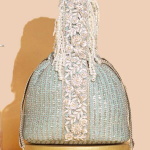 May include: A light mint green drawstring pouch bag featuring vertical silver sequin stripes and a central vertical panel adorned with intricate floral embroidery, silver metallic thread, and white pearl bead accents with matching pearl tassels.