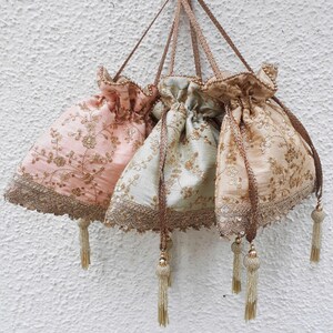 Op de afbeelding: Drie decoratieve trekkoordtassen met gouden borduurwerk en kwastjes. De tassen zijn in tinten roze, groen en beige.