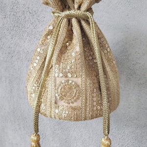 May include: A gold drawstring pouch bag featuring intricate embroidery and dense sequin embellishments. The bag includes a braided gold cord closure with two long, dangling gold beaded tassels at the ends, creating a textured and metallic appearance.